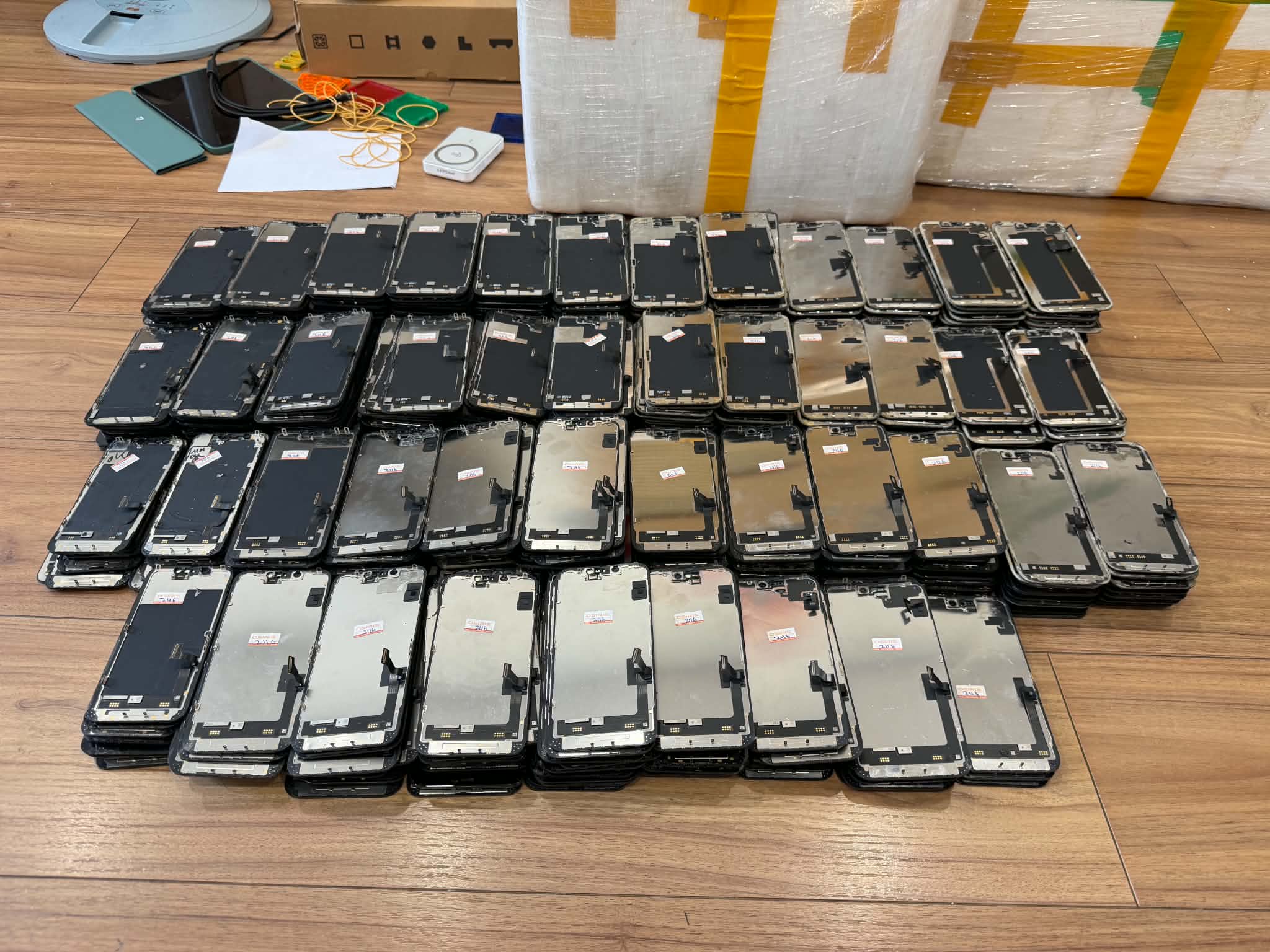Stacks of detached phone screen assemblies arranged on a wooden floor.